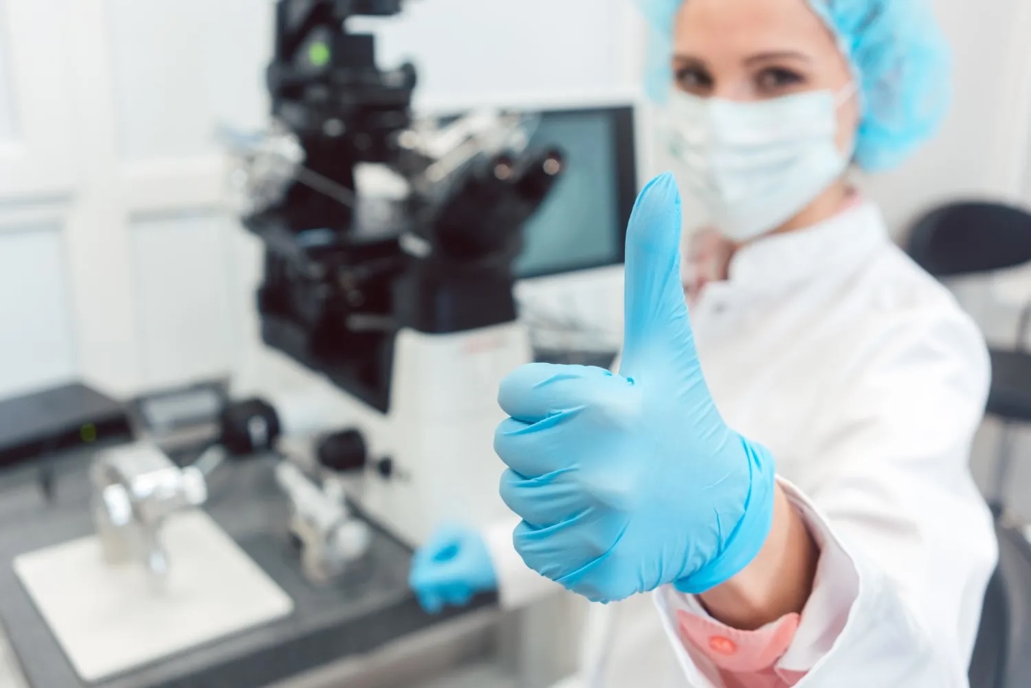 Technicienne de laboratoire dans un centre de PMA levant le pouce après une FIV réussie, incluant transfert embryonnaire, fécondation, DPI et analyse de sperme.
